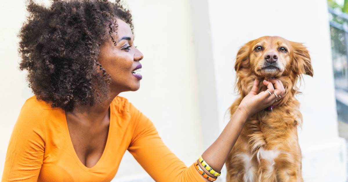 Woman in an orange shirt petting a fluffy brown dog.