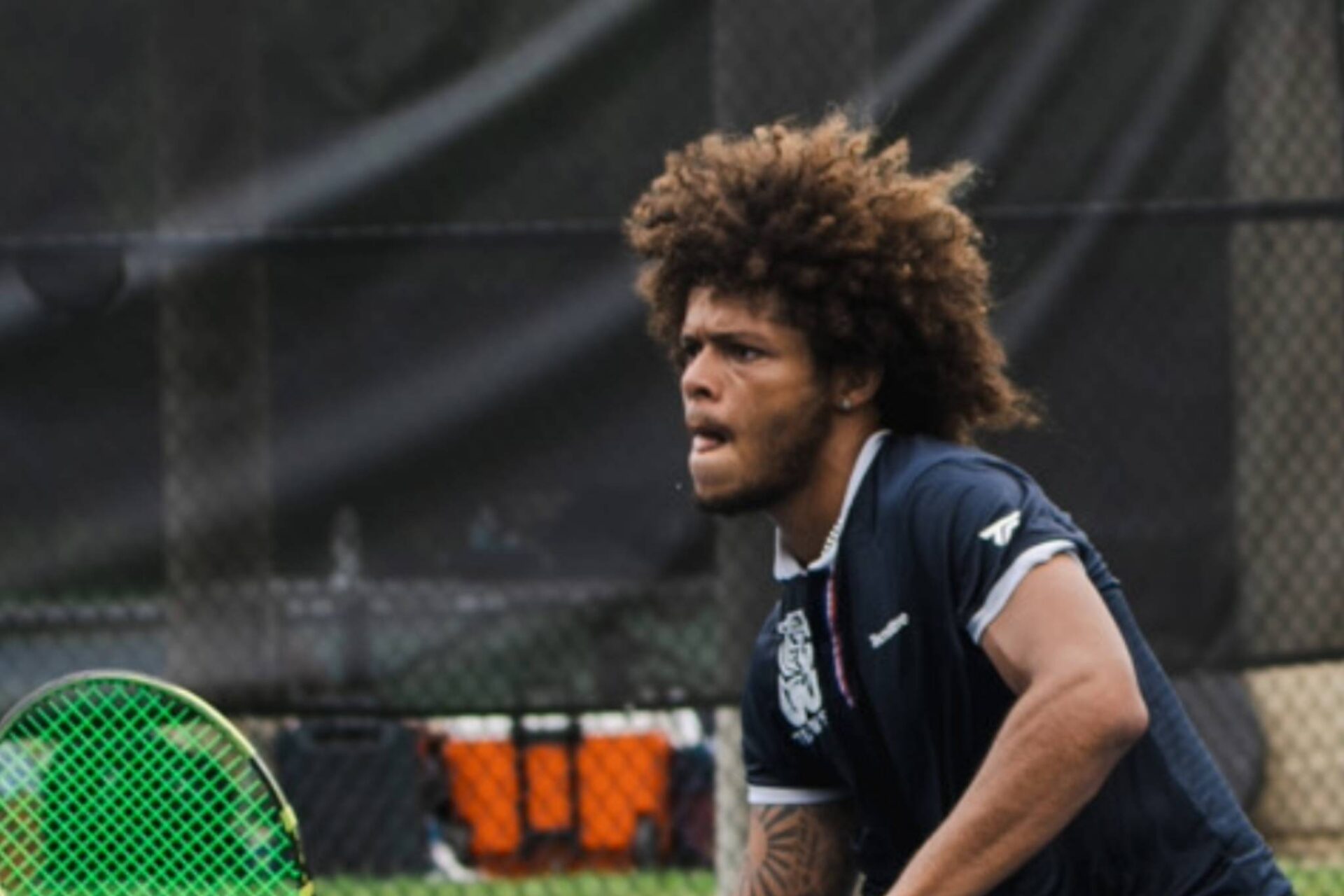A-tennis-player-in-a-dark-outfit-swinging-a-racket-on-a-court-scaled