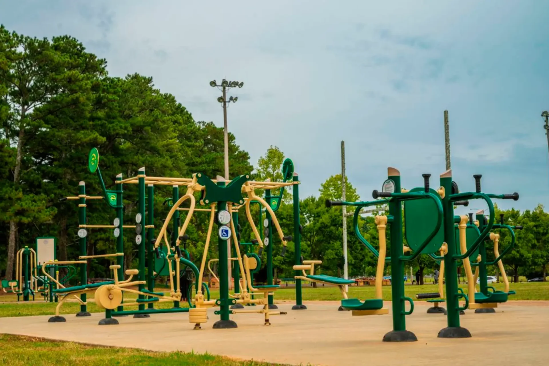 Outdoor fitness area featuring various green exercise machines set against a backdrop of trees and overcast skies